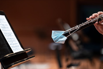 An oboe player in orchestra playing off of sheet music with the end of the instrument covered with a face mask to prevent the spread of a virus - obrazy, fototapety, plakaty