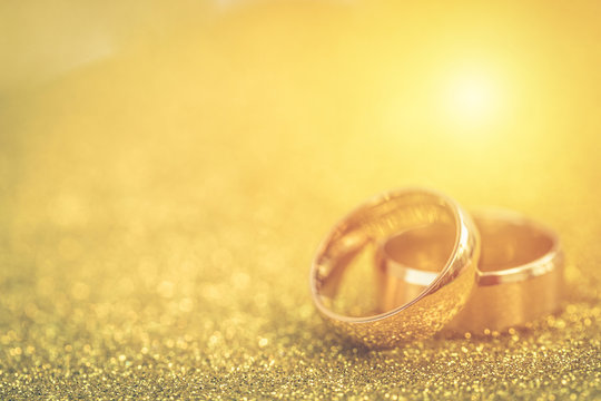 Gold wedding rings of bride and groom on gold gliter