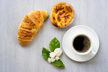 Cup coffee with croissant and bacon quiche on white table.