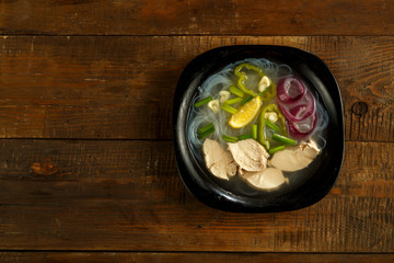 A plate of Vietnamese pho soup with chicken on a wooden table.