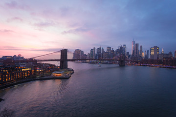 New York City, USA - 26 Dec 2019: Dramatic, colorful Sunset at the East River with Manhattan Skyline Lights and Brooklyn Bridge