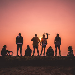 Portrait of a band of 7 musicians from back and a stone pile silhouette and the purple and orange sunset and sun from the mountain, Chile