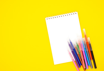 multi-colored markers with a white blank Notepad on a yellow background, space for text