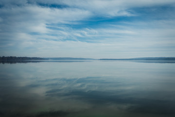 Reflections of Clouds in the Sky on calm, tranquil Water with Trees on Horizon and plenty of Copy Space