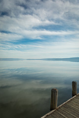 Reflections of Clouds in the Sky on calm, tranquil Water with wooden Pier in Foreground and lots of Copy Space