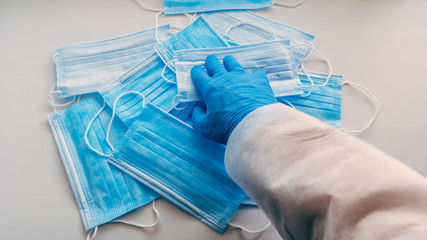 A man in blue medical gloves takes a mask from a pile