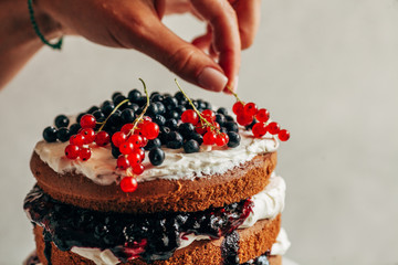 A female hand decorates a cake with fresh berries.