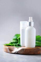 Obraz na płótnie Canvas Natural spa, herbal cosmetics. Nettle lotion, cream, shampoo or soap in white bottle and fresh nettles leaves on grey background. Medicinal herb for health and beauty, skin care and hair treatment.