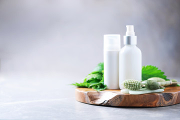 Obraz na płótnie Canvas Face jade roller massager, nettle lotion, cream, shampoo in white bottles and nettles leaves. Medicinal herb for beauty, skin care and hair treatment. Skincare beauty routine at home bathroom.