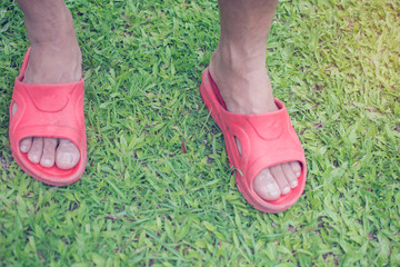 Top view of Asian man feets with red slippers on green grass for relaxation.