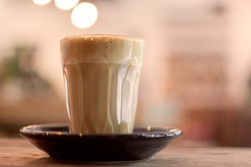 Glass of hot coffee  on a wooden table with bokeh cafe background.