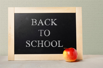 Background of a blackboard in a wooden frame and an Apple on the table with text written in chalk back to school