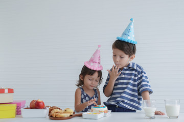 Birthday party in family. Little Caucasian boy and girl wear cute blue pink party hat and enjoy eating cake and milk in birthday party at home 