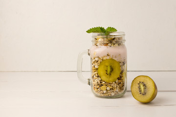 Homemade granola witn kiwi in open glass jar on white wooden background