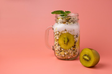 Homemade granola and kiwi in open glass jar on red background