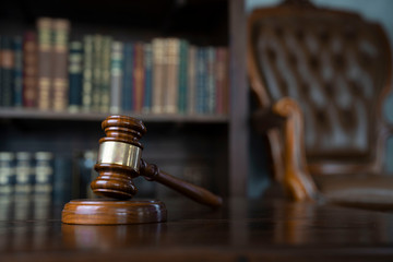 Judge office. Gavel on brown shining table and collection of legal books in the bookshelf.