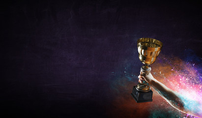 Hand holding up a gold trophy cup against dark background