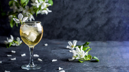 Apple alcoholic cocktail with sparkling wine in glass on a dark background. Refreshing cool summer drink, lemonade or ice tea decorated with apple tree petals. Copy space for text, low key