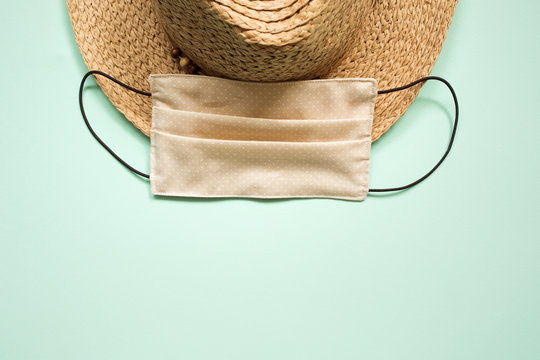 Summer 2020 Concept: Straw Hat And Mask On Plain Mint Background. Coronovirus Covid Holiday Travel Trip