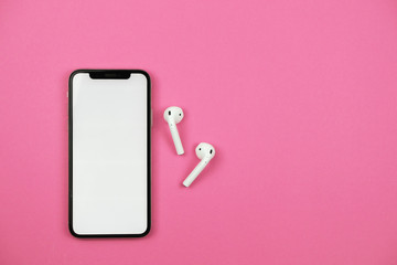 Mobile phone with wireless headphones on pink background.