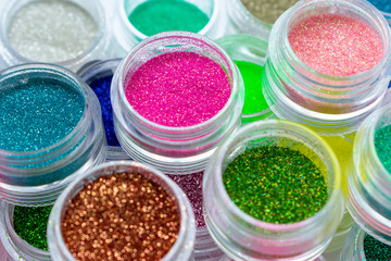 Trendy multicolored glitter in jars. Shimmer, sparkle for makeup, manicure. Shiny powder. Bright pigments. Cosmetic products. Vibrant eye shadow. Blue, pink, green, red, yellow. 