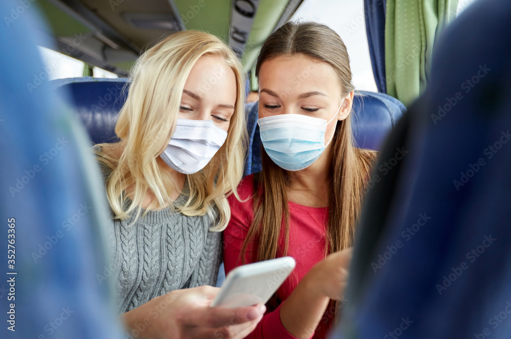 Wall mural tourism, pandemic and health care concept - young women or friends wearing face protective medical mask for protection from virus disease in travel bus texting or reading message on smartphone