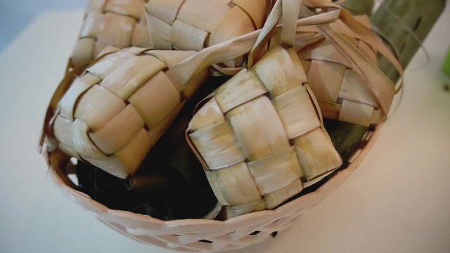 Cinematic shot of popular Malay traditional food, Ketupat rice and Lontong Nasi Impit in one basket. Ketupats, a natural rice casing made from young coconut leaves for cooking rice. Slow motion video.
