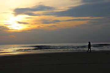 Fototapeta na wymiar person / woman silhouette at the beach under yellow sunrise sun horizon. wavy beach. Dark foreground. tranquil lonely walk along the beach.