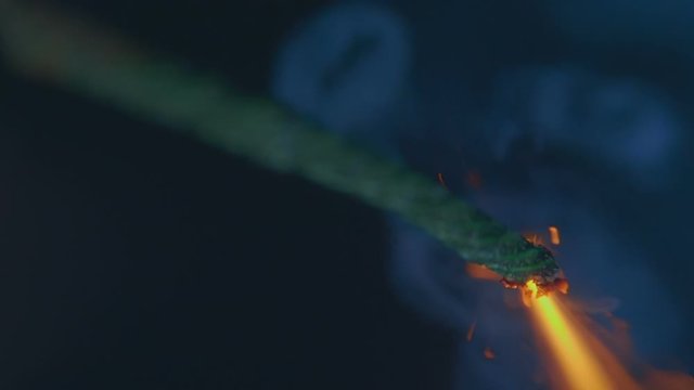A bright stream of fire, sparks and smoke from a lit wick, which is supposed to detonate a bomb or pyrotechnics at a holiday, on a black background. Macro. Closeup. Shallow depth of field. Slow motion