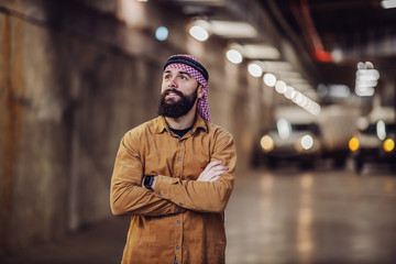 Young proud smiling muslim investor with headscarf standing in building in construction process with arms crossed and looking up.