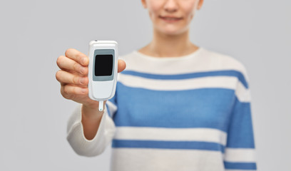 health, medicine and diabetic concept - happy smiling teenage girl with glucometer over grey background