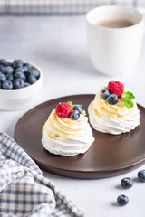 Coffee mug and Pavlova cake with whipped cream and fresh berries on wooden plate. Romantic breakfast