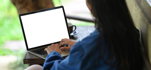 Woman typing on white blank screen computer laptop that putting on wooden working desk while...