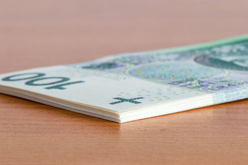 Stack of 100 PLN banknotes on wooden table.