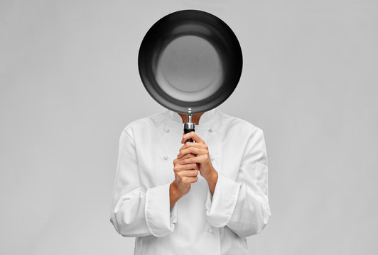 cooking, culinary and people concept - female chef covering her face or head with frying pan over grey background