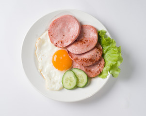 Fried sausage with fried eggs on a plate. Near lettuce leaf and fresh cucumber