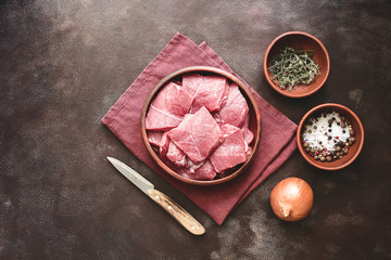 Slices of raw fresh beef meat with spices and herbs on a dark rustic background. Top view, flat lay, copy space.
