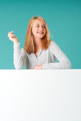 Happy emotional Caucasian girl standing behind an empty white banner, gesturing against a turquoise background
