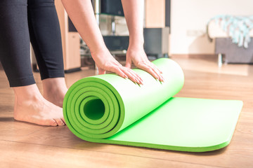 Woman rolling her Yoga mat at home after a training on wooden floor. Concept healthy lifestyle, sport
