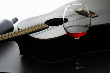 Guitar and high glass with red wine on a stone background.