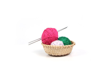 clews of different colours and knitting needles in wicker basket isolated on white background