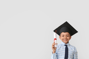 Little African-American boy in graduation hat and with diploma on grey background