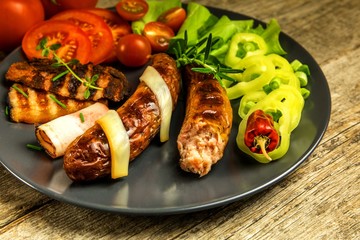 Grilled sausages with bacon and cheese on a black plate. Vegetables for meat. Home preparation for a party.