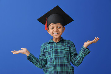 Little African-American boy in graduation hat on color background