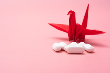 A pile of white pill on a pink rose gold background with a red origami bird
