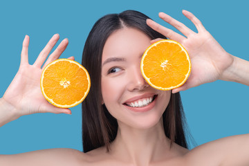 Smiling cute young woman holding slices of orange
