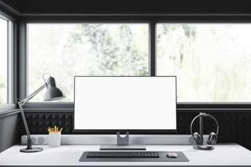 Modern workplace with a blank computer monitor, keyboard, mouse and headphones in front of the window at home or in the studio. Mock up. 3d rendering