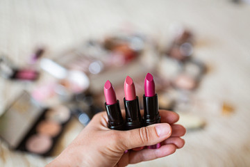 Female hand holding three lipsticks pink color