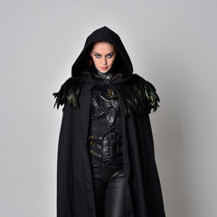 Close up fantasy portrait of a woman with red hair wearing dark leather assassin costume with long black cloak.  isolated against a studio background.