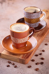 Two cups of espresso coffee on a wooden cutting board and coffee beans